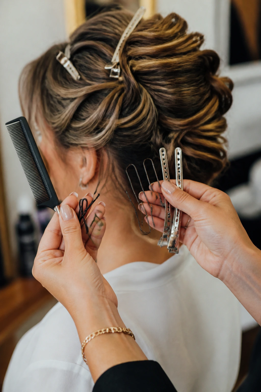 Hands with hair tools in foreground and pinned hairstyle in background