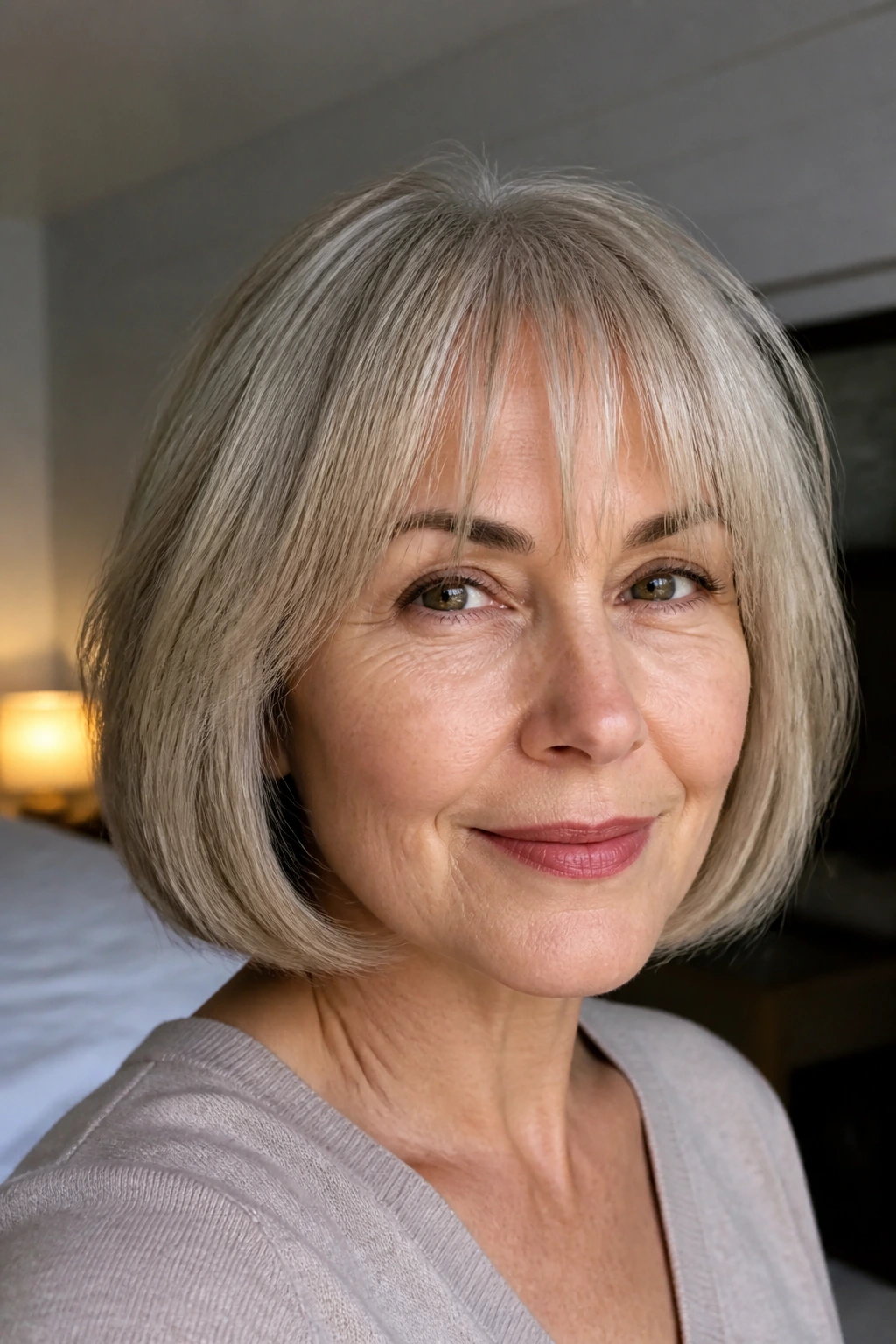 Close-up of a real woman with a bob and wispy bangs in soft natural window light.