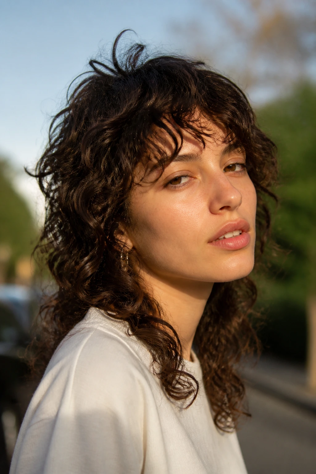 Close-up portrait of a real person with a medium curly wolf cut showing lift at the crown.